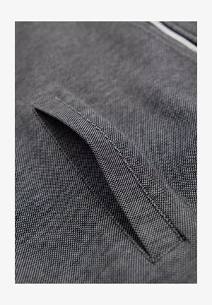 Grijze stof met een gestructureerd oppervlak en een gestikte pocketopening. Het ontwerp is slank met subtiele details en een schone afwerking.