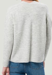 Pull en tricot gris clair avec texture côtelée, encolure arrondie et épaules légèrement tombantes. Associé à un jean en denim bleu.