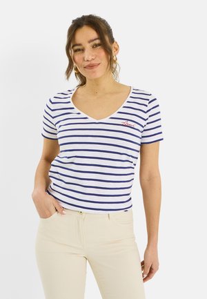 Mujer que lleva una camiseta blanca de cuello en V con rayas horizontales azules y "Amour" bordado en rojo, combinada con pantalones beige claro.
