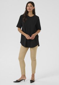 Sort, kortærmet t-shirt med rund halsudskæring, parret med beige slim-fit bukser og sorte hælede mules med sløjfedetaljer.