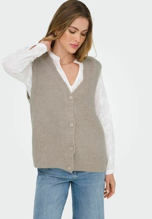 Gilet in maglia beige con scollatura a V, con cinque bottoni sulla parte anteriore e texture a costine. Indossato sopra una camicia bianca con dettagli floreali.