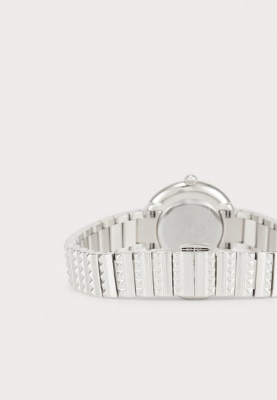 Sidabrinis metalinis laikrodis su tekstūruotu dirželiu, kuriame dera piramidinės ir lygios grandinėlės, apvalus korpusas ir paprastas užsegimas.