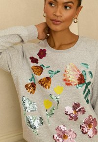 Szara bluza z kwiatowymi wzorami z wielokolorowych cekinów, zawierającymi różne kwiaty i liście, z prążkowanym dekoltem i mankietami.