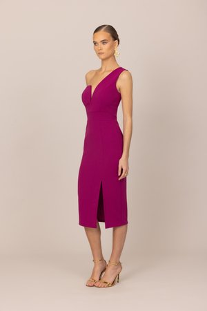 Kvinne som står og har på seg en ermeløs, asymmetrisk magentafarget midikjole med frontsplitt, gullfargede remmesandaler, gulløreringer og ringer.