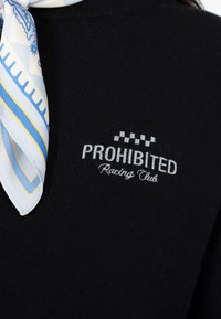 Czarny sweter z wyhaftowanym białym napisem "PROHIBITED Racing Club" i wzorem w kratkę powyżej. Do tego dołączony jasnoniebieski, wzorzysty szalik.