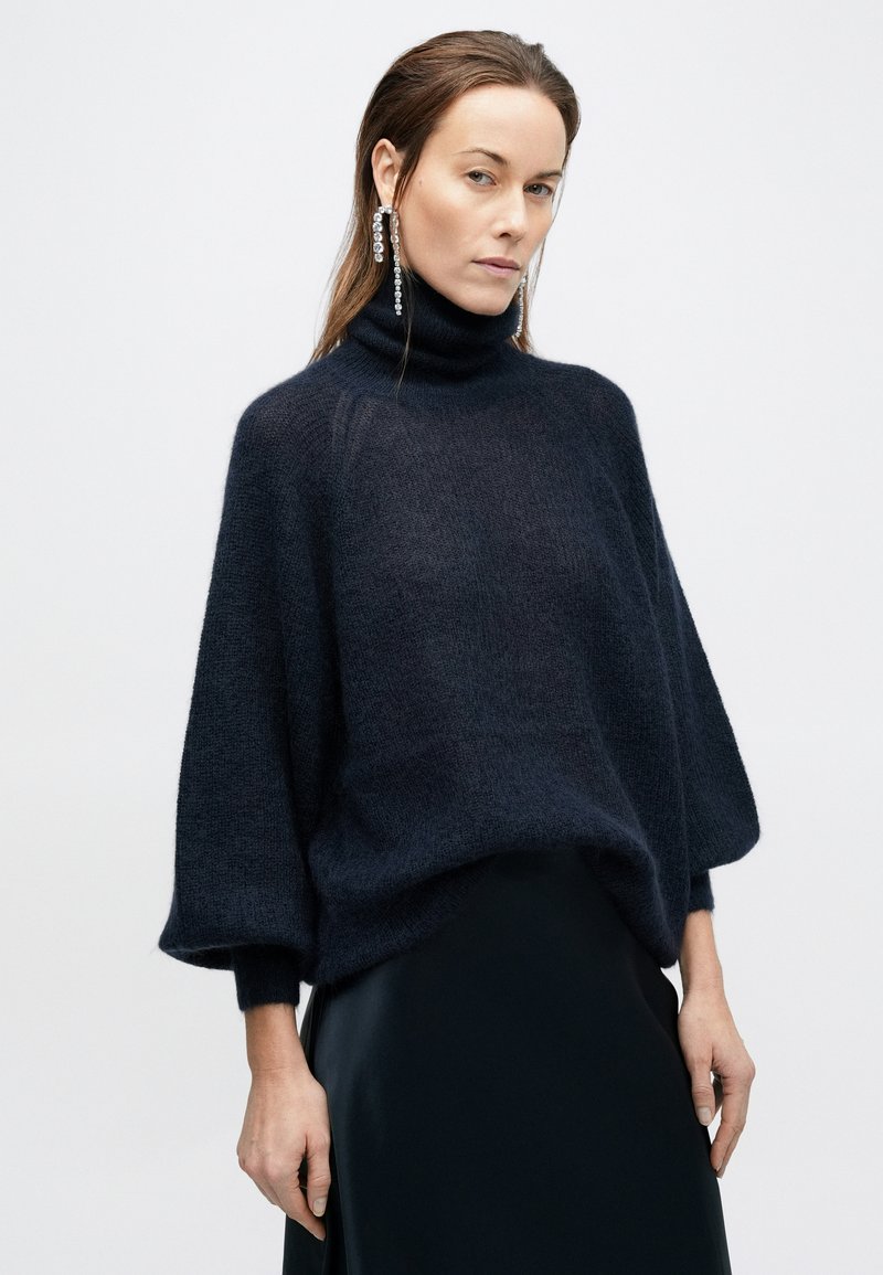Dark navy turtleneck sweater made of a soft, textured knit, featuring wide sleeves and relaxed fit, paired with a sleek black skirt.