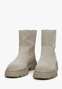 Beige suède enkellaarsjes met een gestructureerde chunky zool, voorzien van een brede opening en een gladde afwerking. Accenten omvatten subtiele stikdetails.