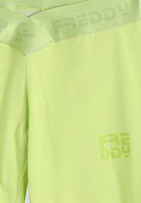 Leggings de color amarillo neón con una textura suave, que incluyen un estampado de logo y una pretina ancha con el nombre de la marca grabado de forma sutil.