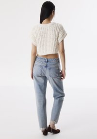 Gestricktes, kurzes, cremefarbenes Oberteil mit einem strukturierten Muster; kombiniert mit hellblauen, lässig geschnittenen Jeans mit ausgefransten Säumen und zwei Gesäßtaschen.