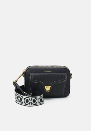 Sac bandoulière en cuir noir avec fermoir doré, coutures blanches et large bandoulière en tissu noir et blanc à motifs sur fond uni.
