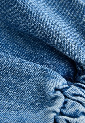 Denim tkanina svijetloplavog do srednje plavog tona, s teksturiranim tkanjem i naglašenim detaljima, prikazujući mekanu, pomalo ugužvanu površinu.