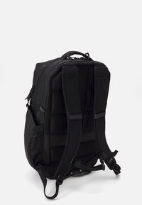 Svart ryggsekk med polstrede stropper og bakpanel, med flere rom, glidelåslukkinger og mesh sidelommer. Teksturet stoff.