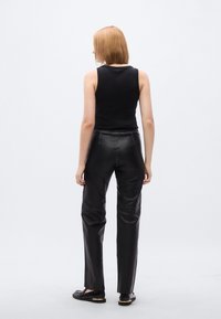 Μαύρο μπλουζάκι χωρίς μανίκια σε συνδυασμό με εφαρμοσμένο μαύρο δερμάτινο παντελόνι. Η εμφάνιση χαρακτηρίζεται από μινιμαλιστικό σχεδιασμό και ομαλή υφή. Μαύρα παπούτσια με χρυσές λεπτομέρειες.