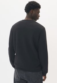 Čierna mikina s okrúhlym výstrihom, ribovanými manžetami a hladkou textúrou. Má zakrivený šev po hornej časti chrbta.