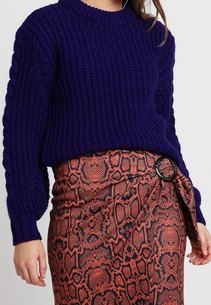 Paarse grofgebreide trui gecombineerd met een hooggetailleerde oranje slangenprintrok met een zwarte ringgesp aan de zijkant.