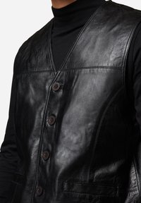 Schwarze Lederweste mit V-Ausschnitt, Fünf-Knopf-Verschluss und Seitentaschen. Glatte Textur mit sichtbaren Nähten und figurnaher Passform.