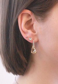 Goldfarbene Ohrringe mit einem klaren, tropfenförmigen Edelstein und zwei kleinen Ohrsteckern, einer mit Kristallakzent und einer metallic.