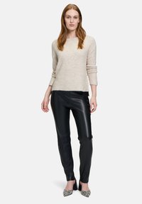 Hellbeige gestrickter Pullover mit langen Ärmeln, kombiniert mit schwarzen Lederhosen und gemusterten High Heels. Einfaches, modernes Design.