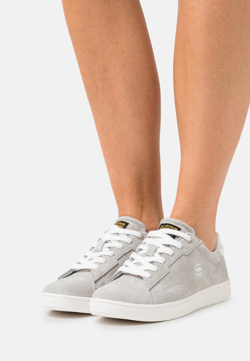 Gray suede sneakers with white laces and a white rubber sole. Features a logo on the side and a padded collar for comfort.