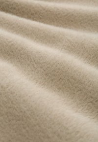 Lichtbeige wol stof met een zachte, textuurrijke oppervlakte en subtiele plooien, die de warme, fuzzy uitstraling benadrukken.