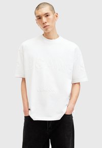 White cotton T-shirt featuring raised text "SAINT LONDON" in matching color. Boxy fit with short sleeves and crew neckline.