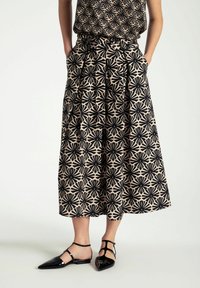 Zwarte en crèmekleurige rok met bloemendessin, geplooid ontwerp en zakken. Gecombineerd met zwarte puntige flats met enkelbandjes.