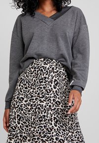 Sudadera gris de cuello en V con corte holgado, combinada con una falda crema que presenta un patrón de estampado de leopardo en negro y marrón.