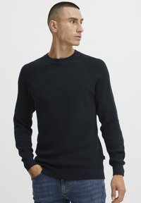Pulover bleumarin cu aspect nervurat, cu gât rotund și mâneci lungi, având un design ajustat și slituri laterale, purtat cu blugi albaștri.