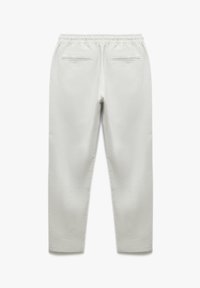 Witte broek met een gestructureerde afwerking, voorzien van een elastische tailleband en twee achterzakken met rits, die toelopen bij de enkel.