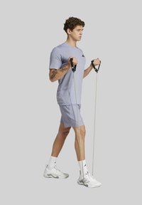 Man in lichtpaarse sportkleding gebruikt weerstandsbanden voor bicep curls, staande op één trede met een gefocuste uitdrukking.