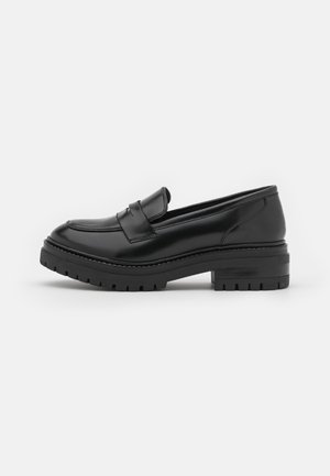 Mocassins en cuir noir avec un bout arrondi, des détails cousus, une semelle en caoutchouc plate et un talon bas empilé. Texture lisse et finition polie.