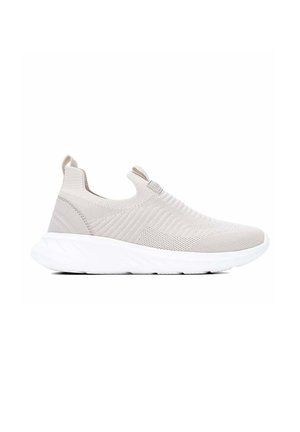 Deportiva beige claro sin cordones con parte superior de punto, lengüetas en la lengüeta y el talón, y suela gruesa blanca acolchada.