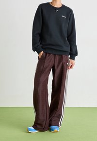 Felpa nera con logo, pantaloni bordeaux a motivi con strisce bianche e scarpe da ginnastica blu con suola testurizzata.