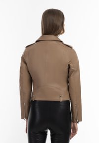 Giacca fitted in ecopelle beige con colletto, polsini con zip e tasche laterali. Il retro presenta cuciture verticali per un design n aggiuntivo.