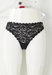String en dentelle noire avec des bords festonnés, orné d'un motif léopard. Présenté sur un support avec un sous-vêtement blanc en dessous.