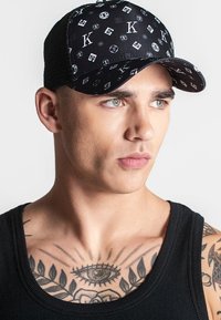 Gorra negra con un patrón de logotipos y símbolos, con una forma estructurada y parte trasera de malla. Tejido texturizado y ala curvada completan el diseño.