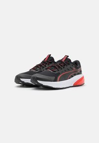 Baskets de sport noires et rouges avec une tige en mesh, semelle intermédiaire blanche contrastante, détails texturés et lacets noirs.
