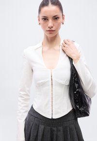 Bijela bluza s dugim rukavima, dubokim V-izrezom i zatvaračem na kopčanje, s pripijenim gornjim dijelom i blago skupljenim dojkama. Teksturirana siva plisirana suknja.