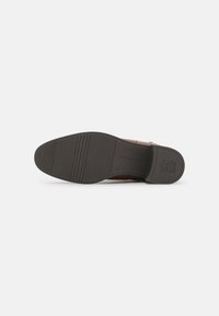 Suela de zapato de cuero marrón con suela de goma negra texturizada, que presenta ranuras horizontales y un logo en relieve. Diseño elegante y simple.