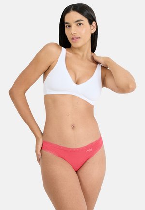 Weißer kabelloser BH mit glatter Textur und V-Ausschnitt, kombiniert mit korallenfarbenen Bikini-Slips mit Spitzenbesatz und Logodetail.