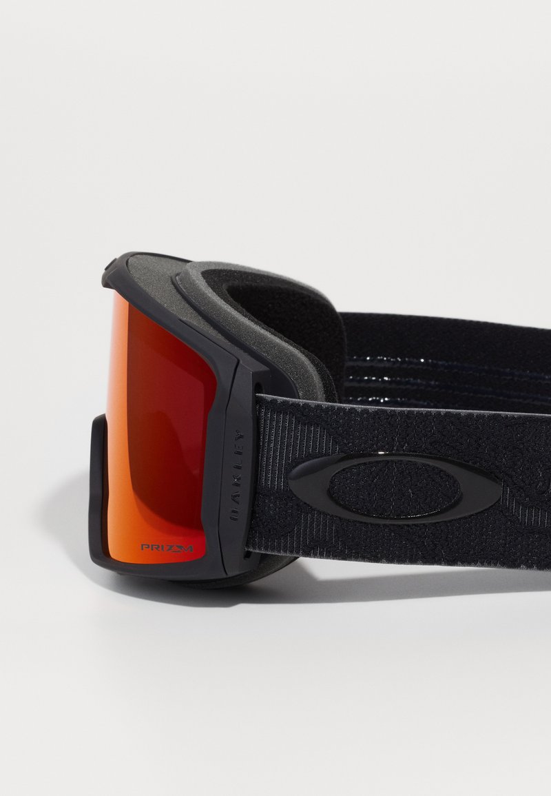 Lunettes de neige avec un grand verre rouge courbé, une monture noire, un revêtement en mousse douce et une sangle en tissu ajustable à motif texturé.