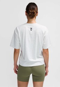 Camiseta blanca de manga corta con textura moteada, que presenta un logo en forma de chevron negro en la espalda. Combinada con shorts de textura verde olivo.