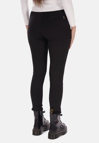 Pantaloni neri aderenti con una texture liscia, caratterizzati da una tasca posteriore e cerniere alle caviglie, indossati con stivali neri stringati.