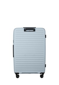 Light blue hardshell suitcase with vertical grooves, black handles, and a retractable handle. Features four wheels for mobility.