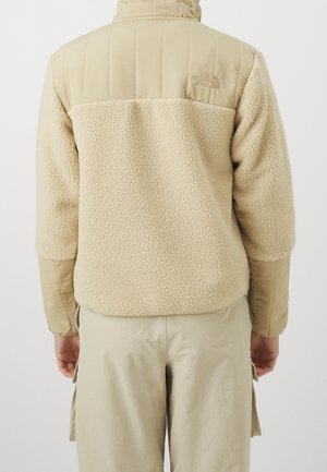 Beige jas met een zachte, gestructureerde fleece body en gladde, satijnglans mouwen; heeft een hoge kraag en een geborduurd logo op de achterkant.