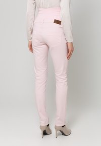 Jeans a vita alta rosa chiaro con una texture liscia, dotati di due tasche posteriori e una etichetta in pelle marrone sulla cintura.