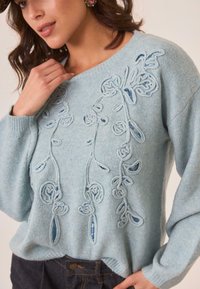 Suéter de punto azul claro con bordado floral y lentejuelas. Presenta un corte holgado, escote redondo y tejido texturizado.