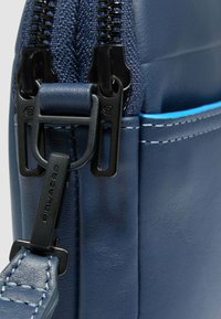 Borsa in pelle blu navy con cerniere e accessori neri. Presenta una superficie testurizzata e cuciture blu in contrasto lungo il pannello della cerniera.