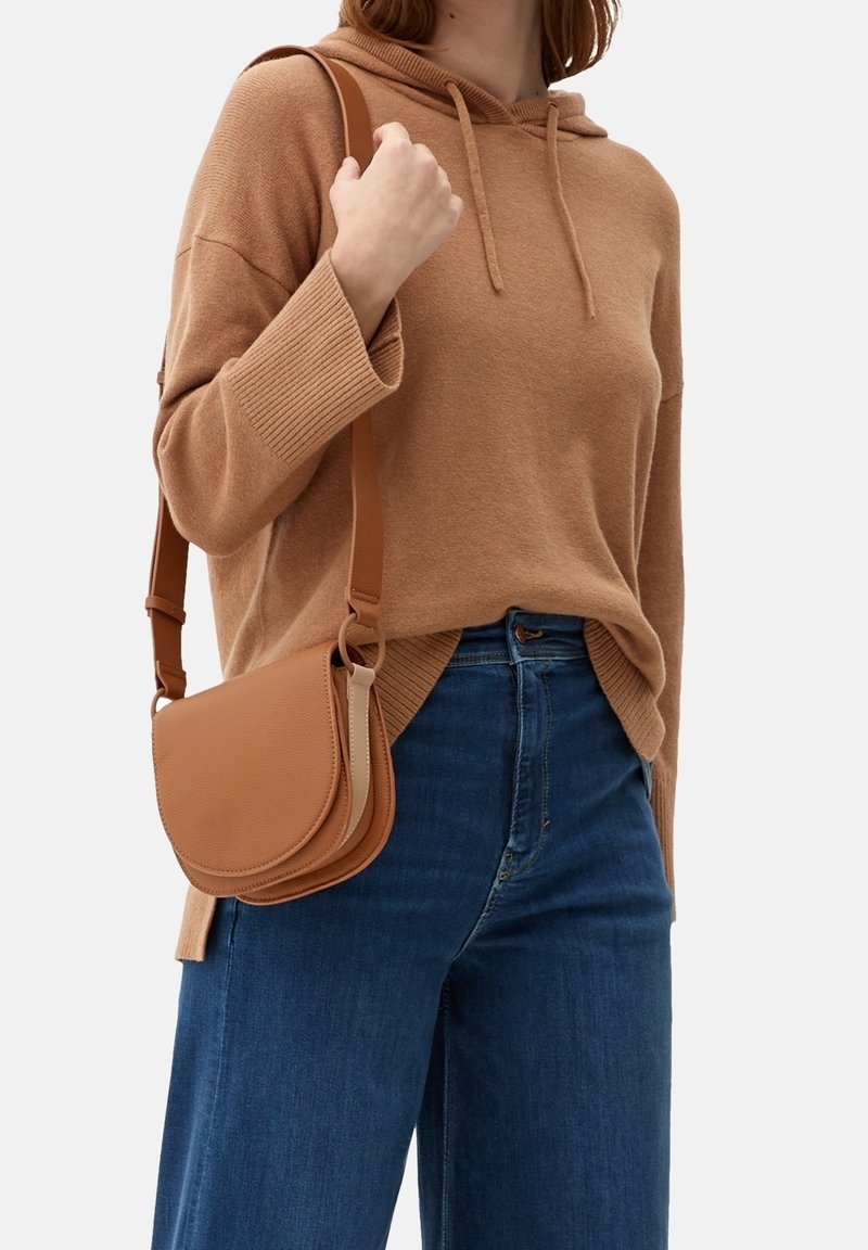 Brun läderaxelväska med en böjd klaffdesign, justerbar rem och texturerad yta. Matchad med en oversized beige tröja och blå jeans.