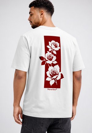 Man wearing white t-shirt with a vertical red rectangle on the back featuring three white roses and the word Neverless below.